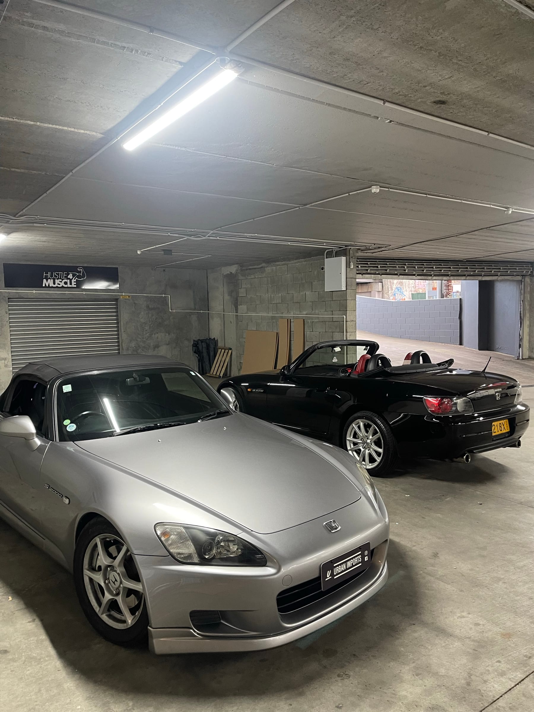 A silver and a black Honda S2000 parked together in the garage
