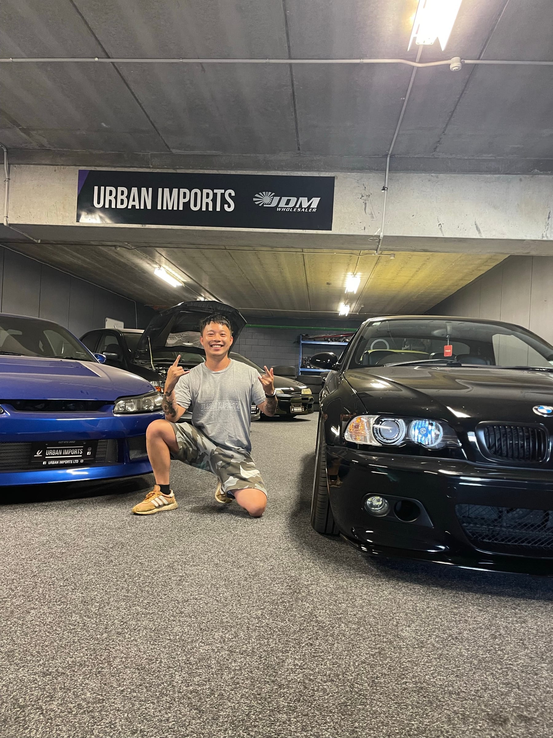 Johny Chhy, founder of Urban Imports, standing between imported cars in the garage