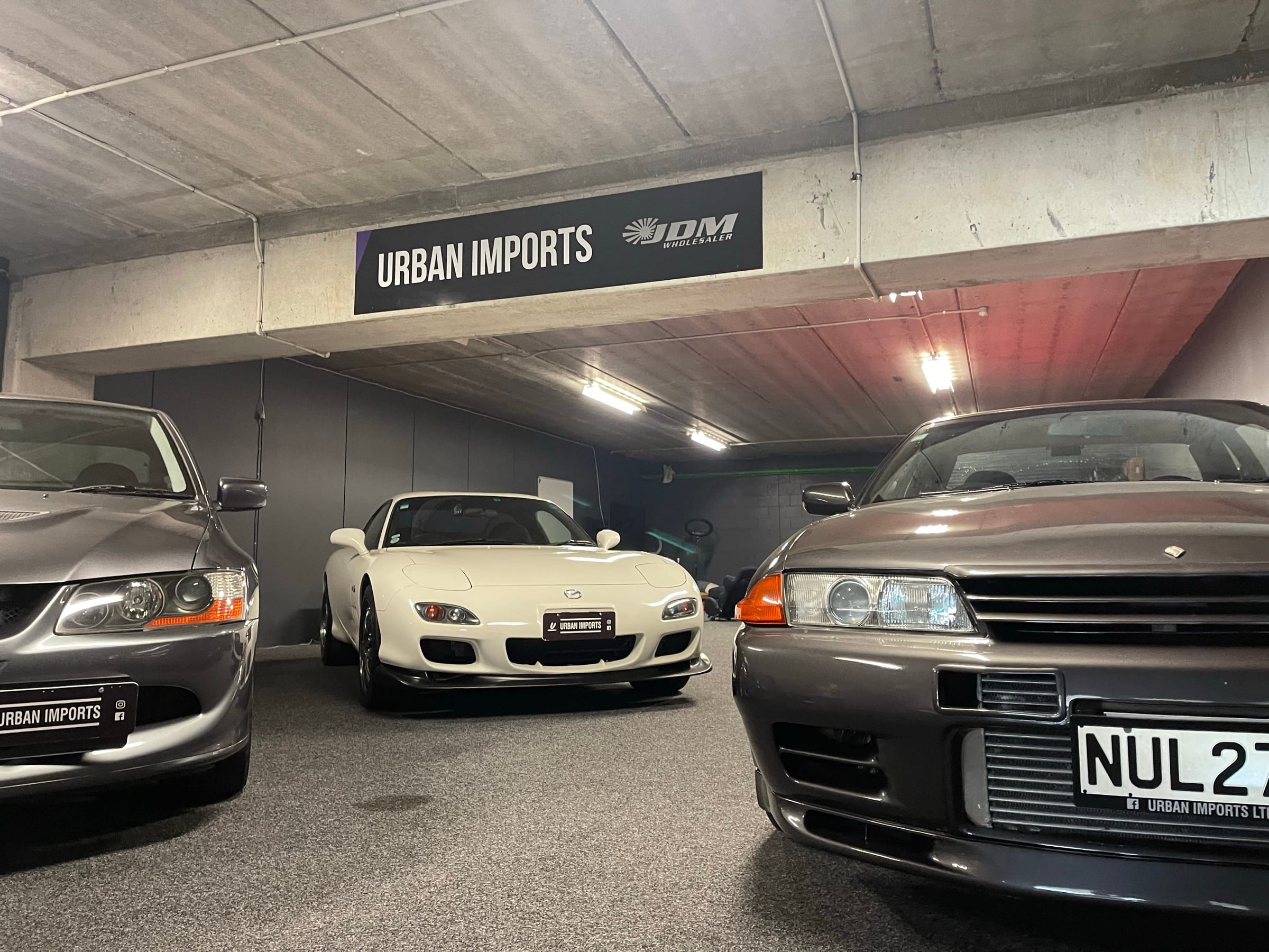 Three imported Japanese performance cars parked under the Urban Imports sign in the Auckland garage