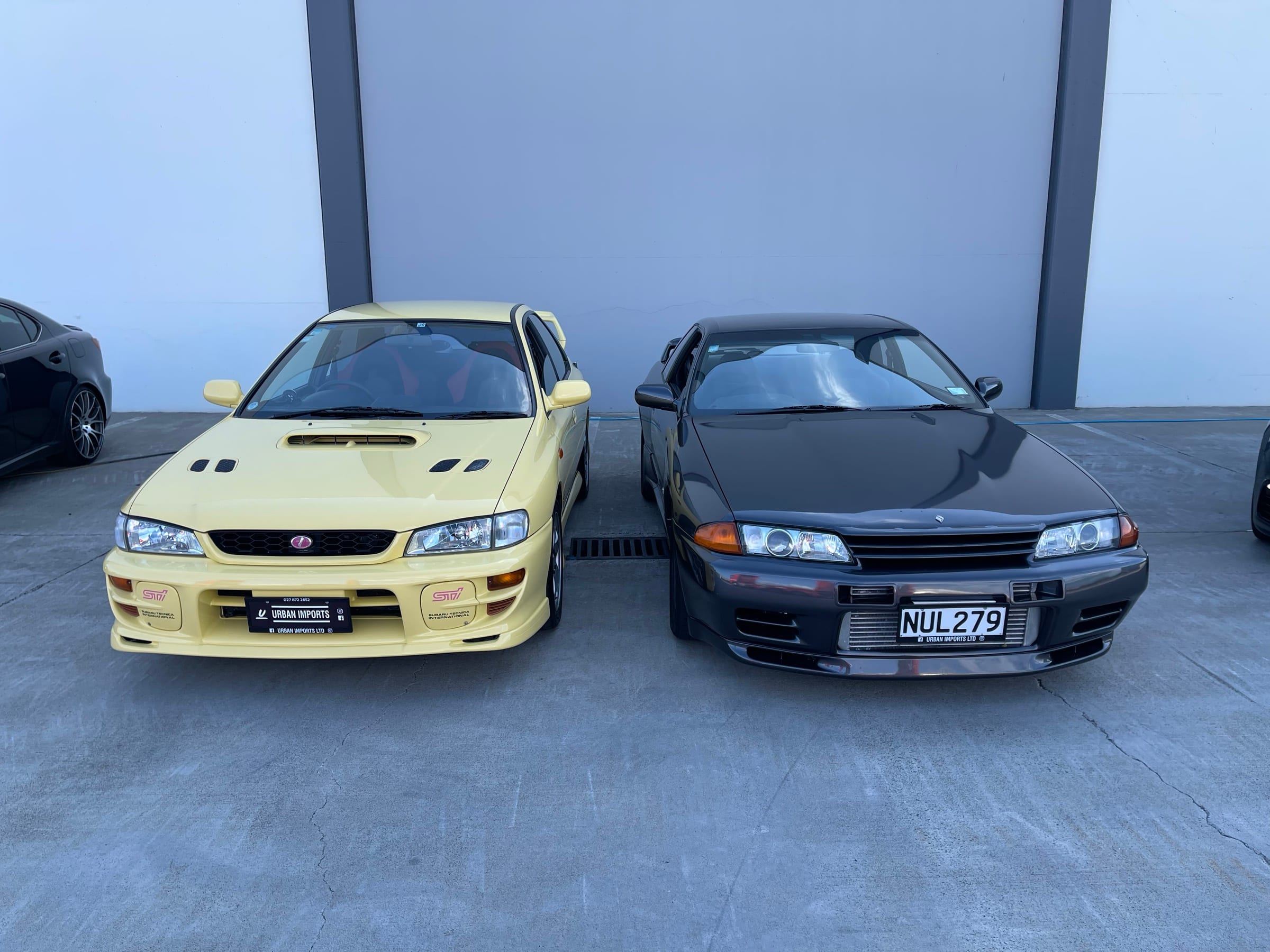 A yellow Subaru Impreza STI parked beside a Nissan Skyline R33